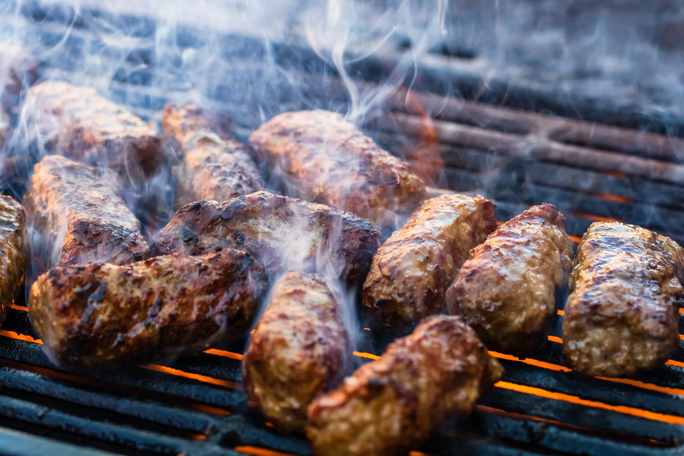 Preparing meat rolls called mici or mititei on barbecue. close up of grill with burning fire with flame and smoke.