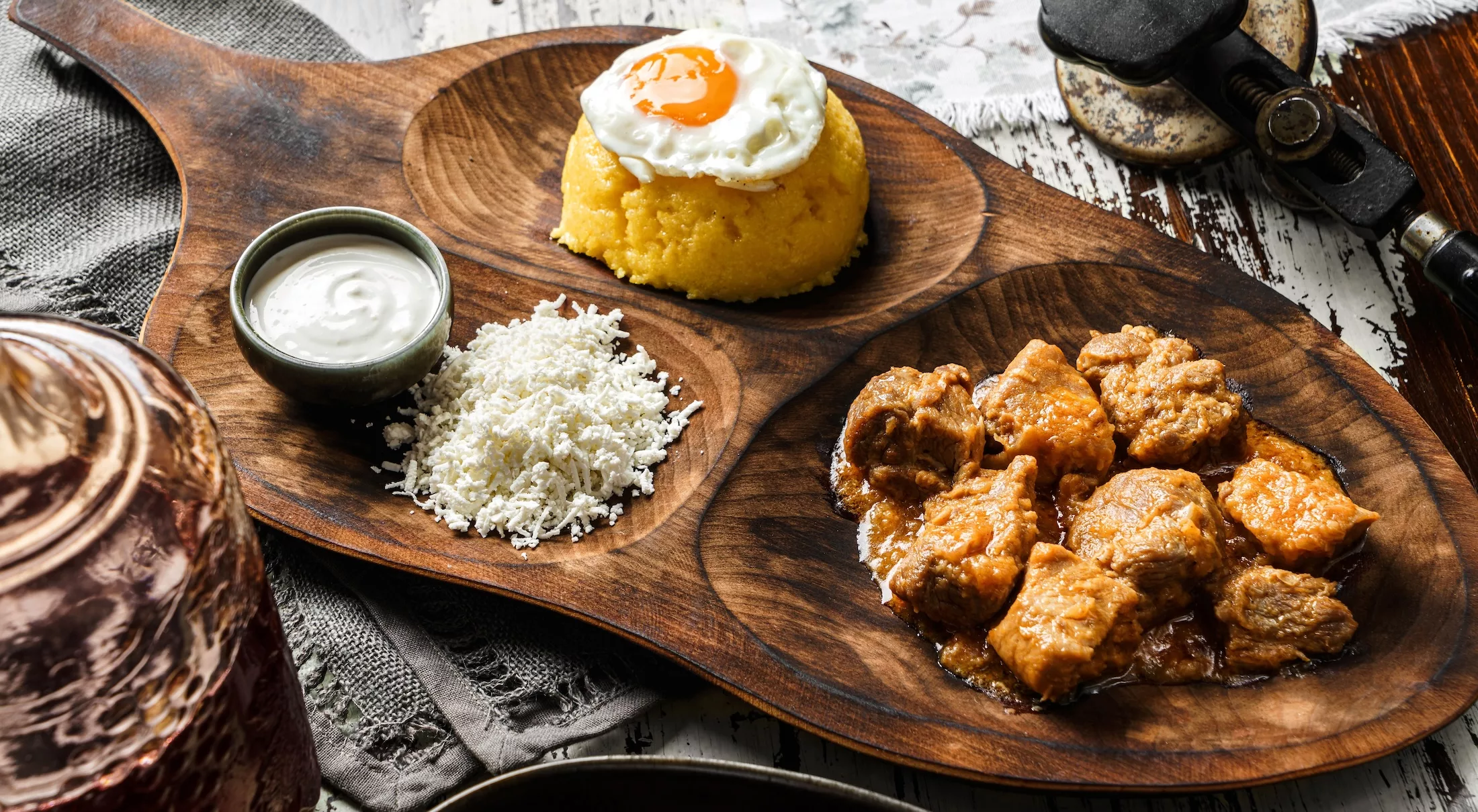 Delicious polenta with fried eggs, cheese, stew meat and sour cream on wooden board over rustic background. Traditional romanian healthy food, top view selective focus