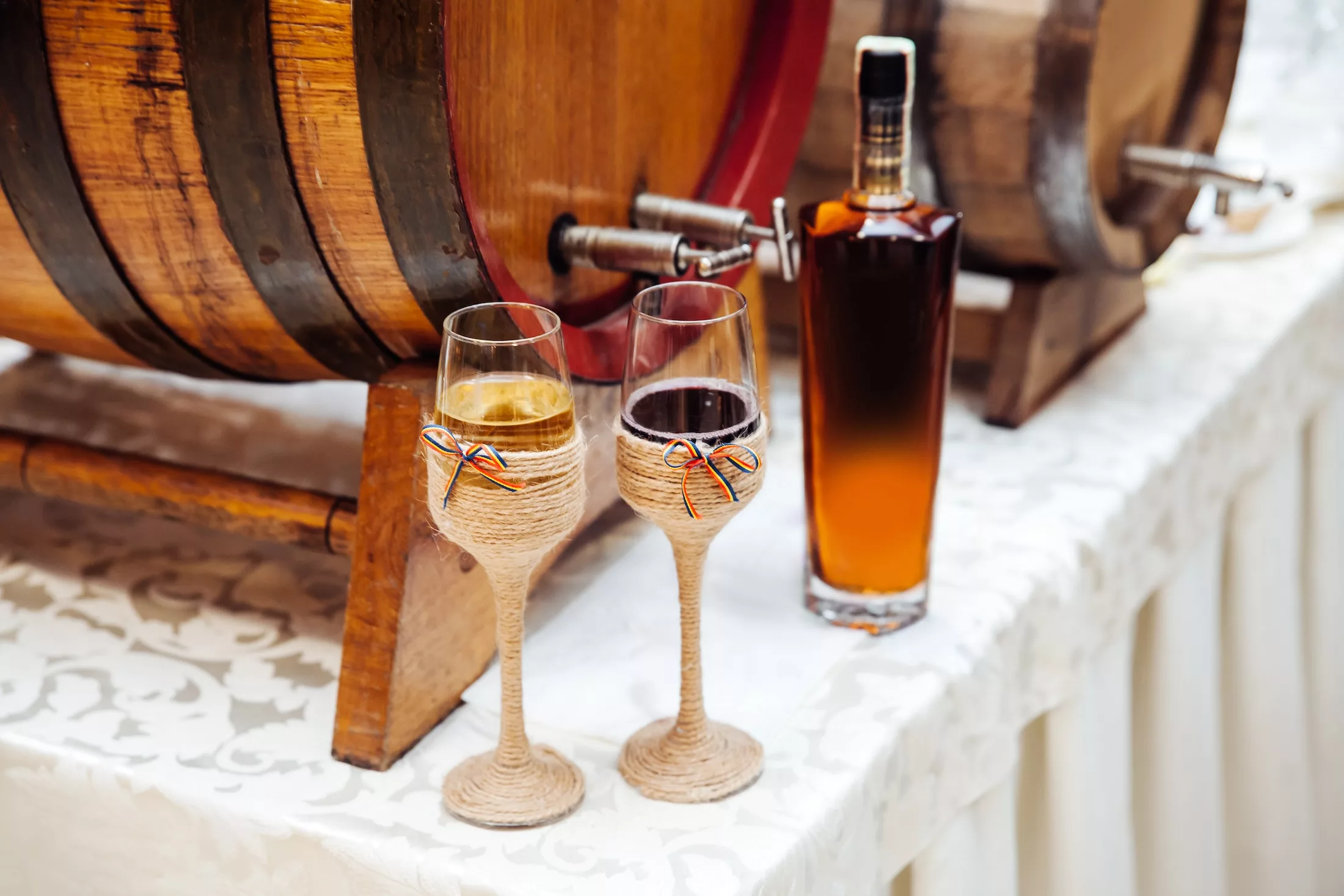 Two glasses with wine ornamented in the Romanian / Moldavian traditional style with the national flag. Various alcohol drinks near wooden barrels.