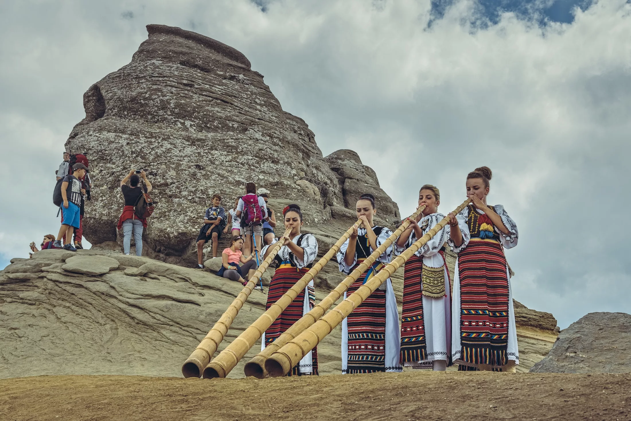Bucegi Mountains, Romania - August 6, 2016: Young Romanian women dressed in colorful traditional costumes play the tulnic near the Sphinx megalith in Bucegi mountains.
